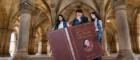 Three students hold an oversized copy of Wealth of Nations in the Cloisters
