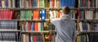 A student looking through shelves of books in the Library