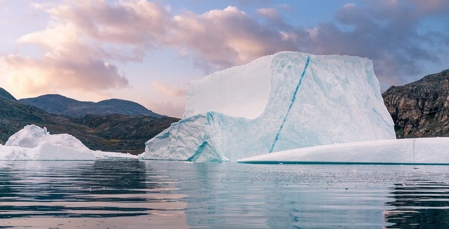 A white and blue iceberg floating on the sea next to bare cliffs and hills. Source: iStockphoto