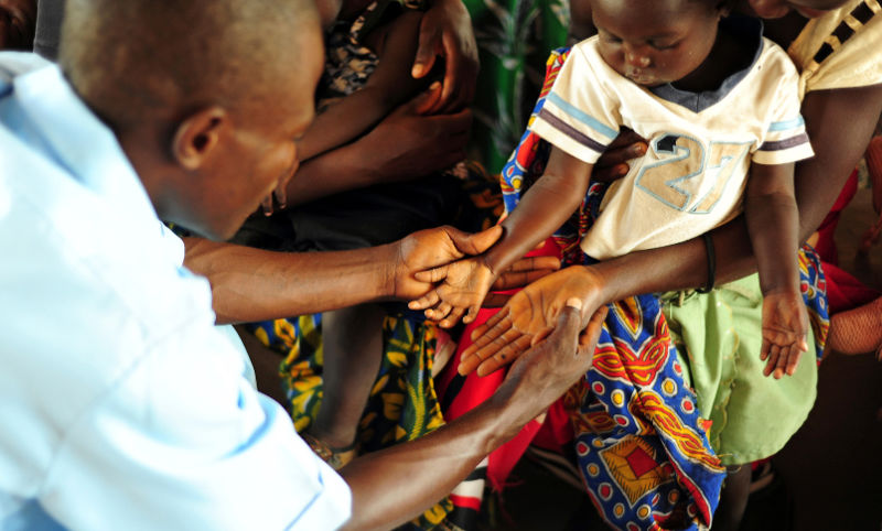 Medical worker holding a child and mothers hands examining them for malaria