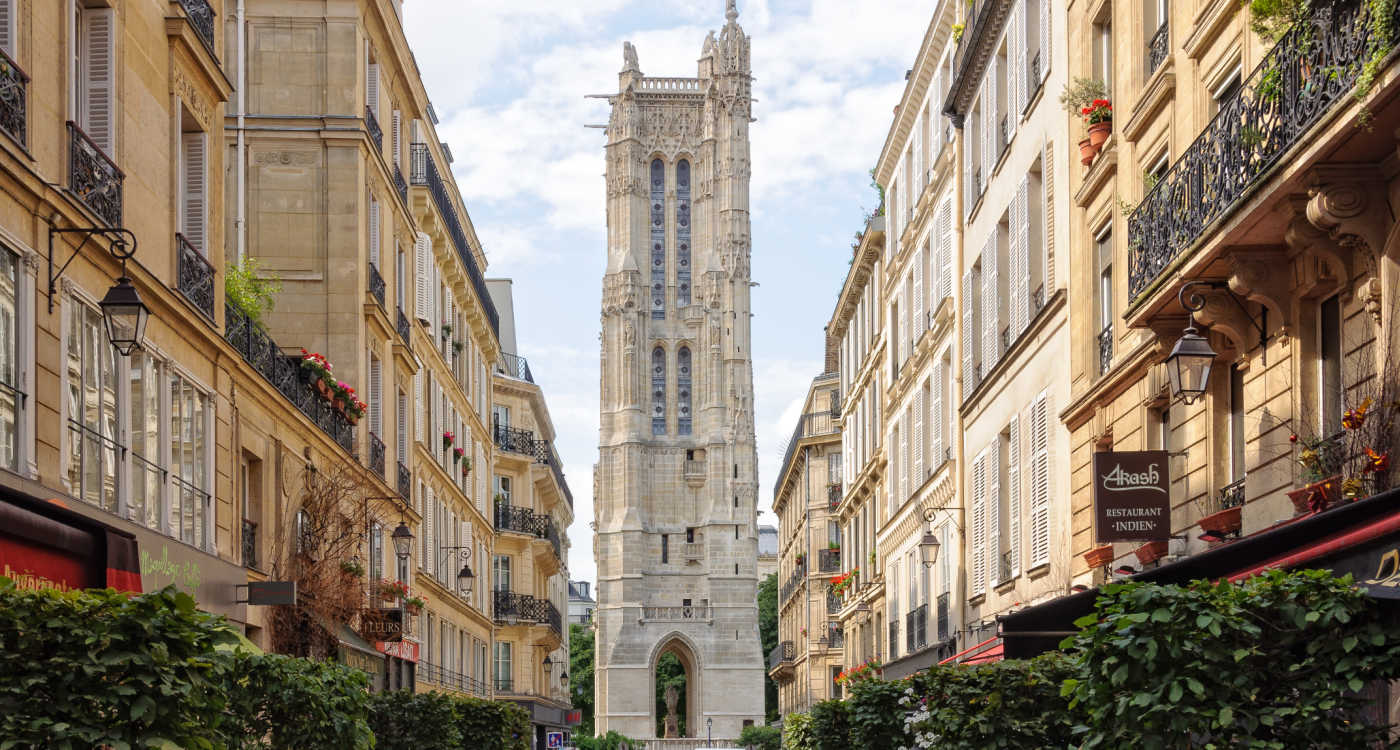 The tall, pale, stone Saint-Jacques Tower viewed along the street, appearing at the end of the road between rows of buildings [Photo: Shutterstock]