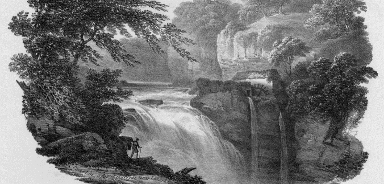 A man overlooking a very large waterfall with a watermill