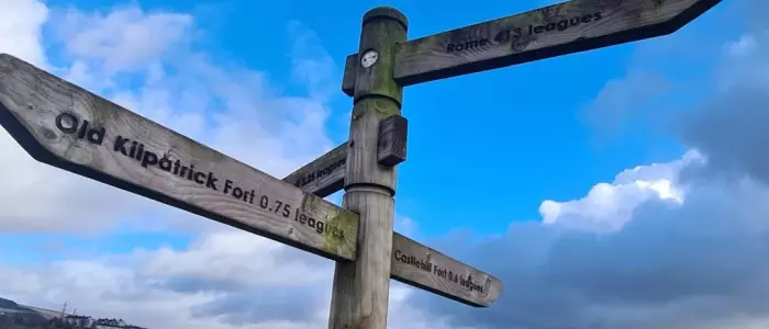 Wooden signpost reading, from top to bottom, 'Rome 413 leagues', 'Old Kilpatrick Fort 0.75 leagues', 'Castlehill Fort 0.6 leagues'