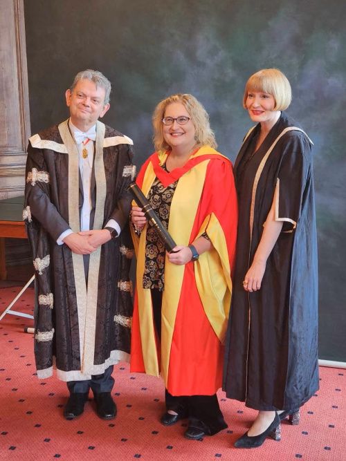Professor Kathy Belov holding her Honorary Doctorate and posing with Professor Sir Anton Muscatelli and Rachel Sandison, all dressed in graduation robes