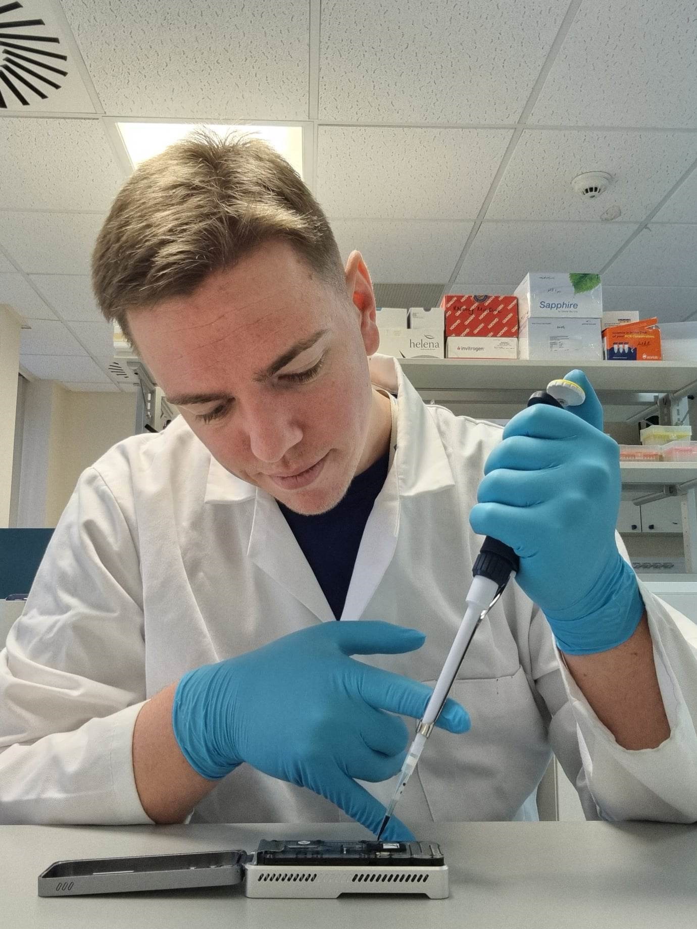 A head and shoulders shot of Dr Nathan Loustalot working in the lab, wearing a lab coat, gloves and holding a pipette