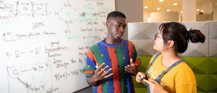 Two students standing in front of a white board with mathematical equations on it