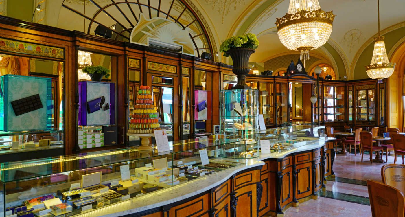 Inside the landmark Café Gerbeaud showing cakes behind glass cabinets and an ornate wooden and mirrored interior [Photo: Shutterstock]