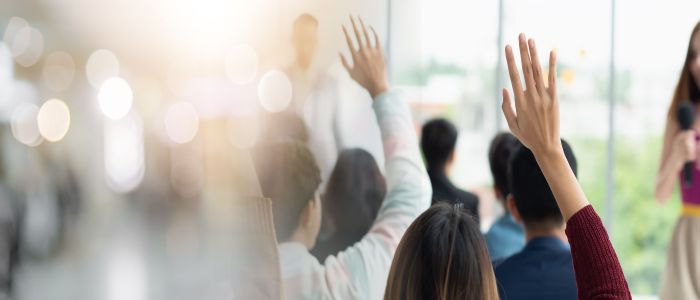 A group at a meeting raising hands for questions