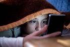 Boy under a blanket looking at mobile screen