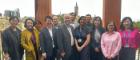 Group photo of guests standing in front of a window with the University of Glasgow tower in the background