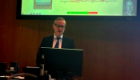 Professor Robert Gray stood at a podium as he delivers his inaugural lecture with a slide visible on the large screen above his head