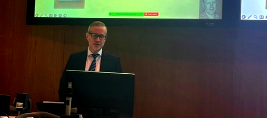 Professor Robert Gray stood at a podium as he delivers his inaugural lecture with a slide visible on the large screen above his head