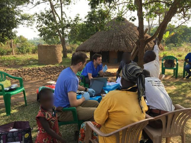 Two doctors in blue scrubs interacting with a group of people in an African setting.