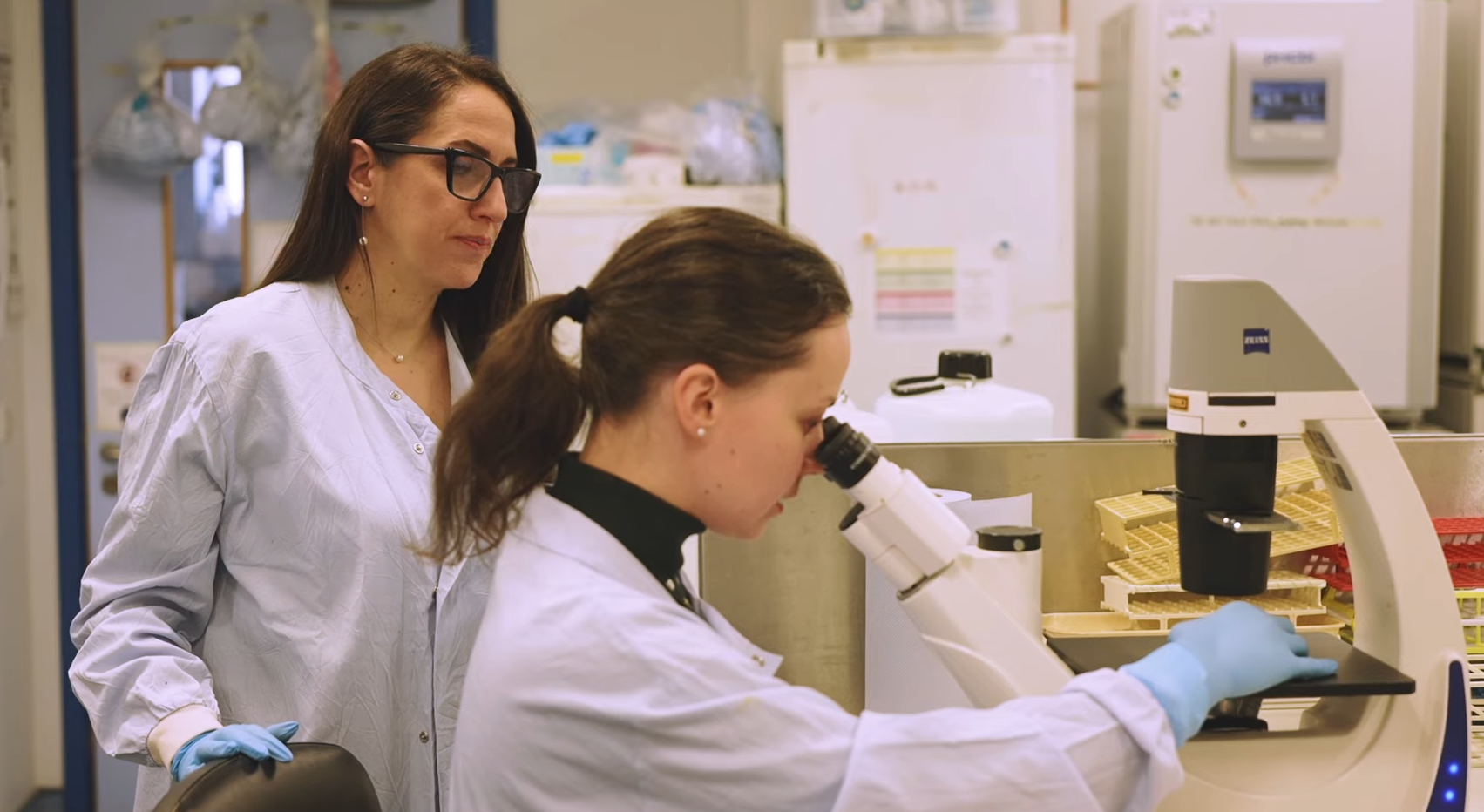 Professor Lilach Sheiner overseeing lab work as a colleague looks through a microscope