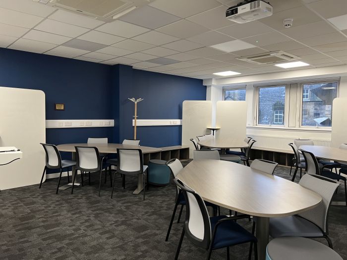 Flat floored teaching room with tables and chairs in groups, projector, and moveable whiteboards.