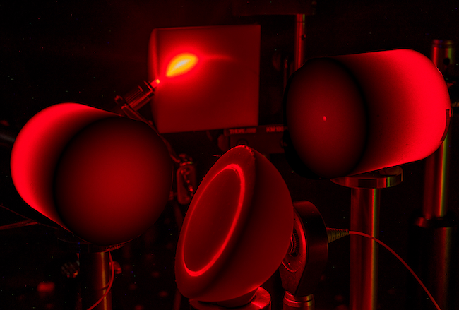 Custom 3D printed white resin semi-cylinder- illuminated by laser (RHS). The resin is printed with an arc channel, and laser light is shone from one side. Diffusive scatter waveguiding occurs, where light is guided out to the other side. Image is a stack of different exposures.