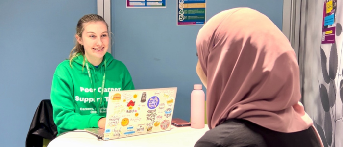 Peer career support student sitting at a desk with another student helping them with career/job questions