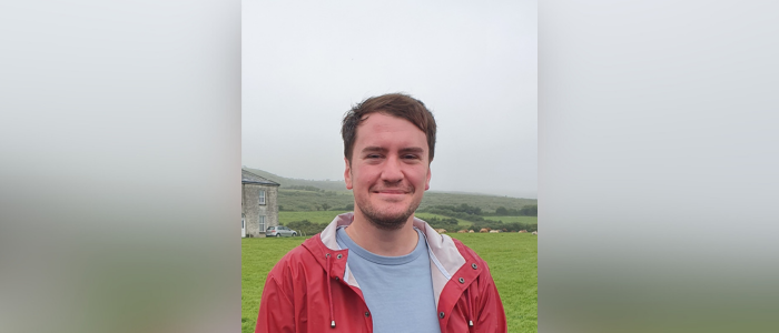 a student standing in a field smiling at the camera