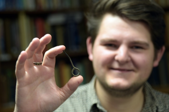 Dr Edward Stewart of the University of Glasgow holds the copper alloy plaid pin found just outside the 17th-century house at Achnacon. Photo: Michael Given.