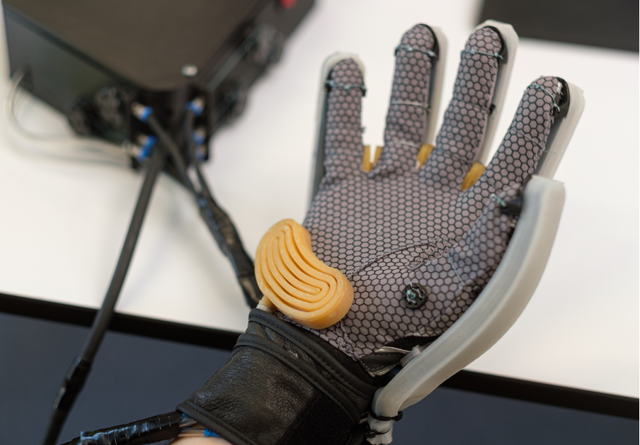 a gloved hand with sensors and actuators connected to a computer in the corner