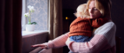 A woman holding her child checks the radiator for warmth