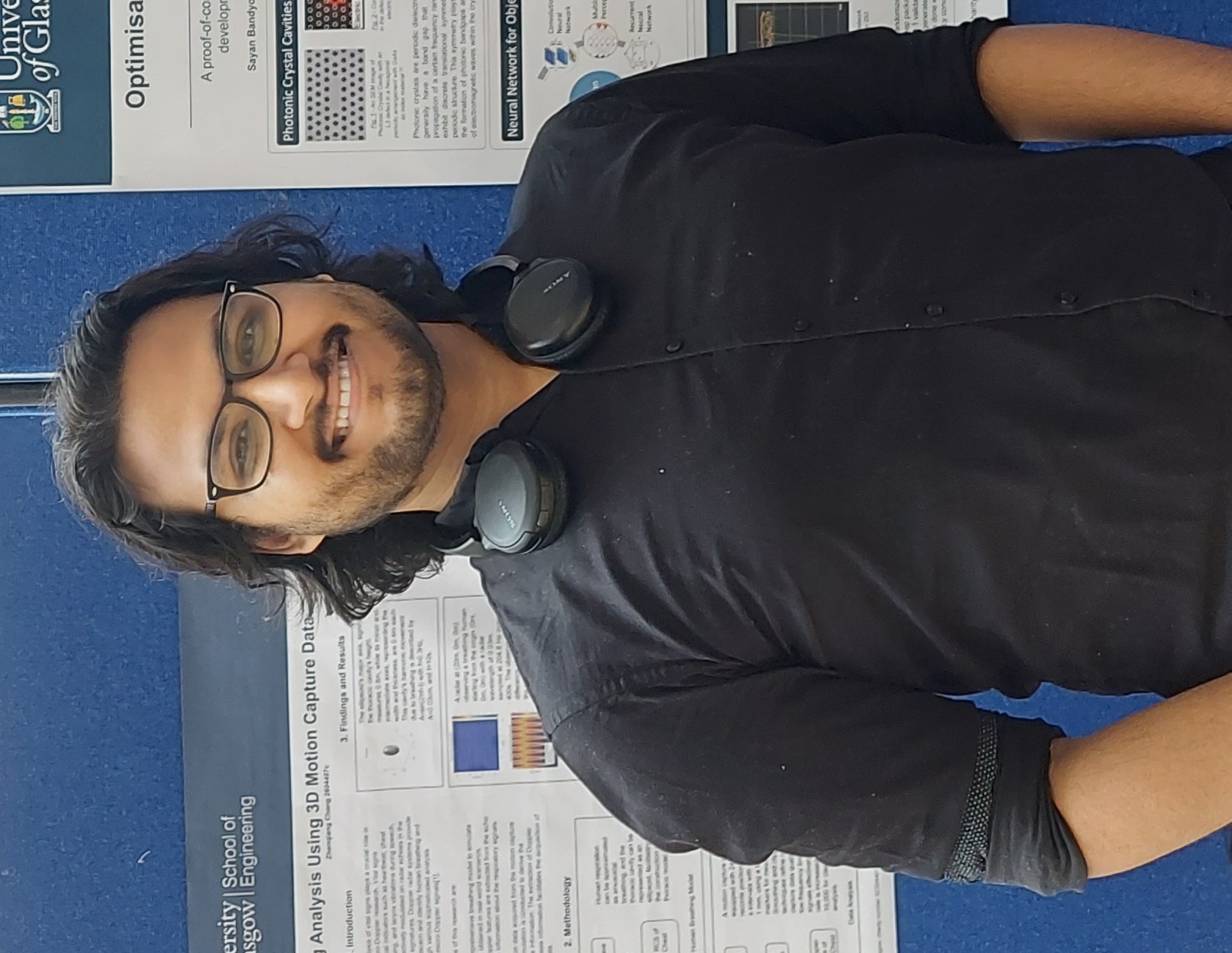 A student wearing black standing in front of a scientific poster presentation with headphones