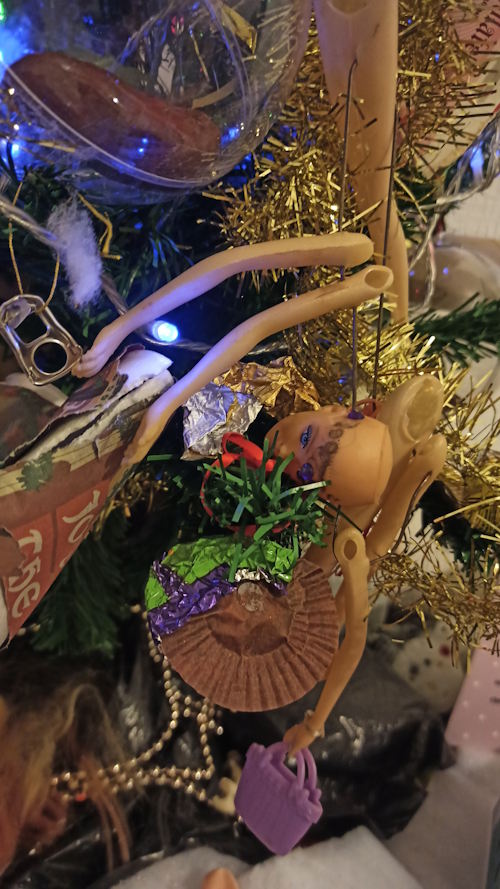 Close up photo of the branches of a Christmas tree decorated with lights, tinsel and assorted rubbish including various body parts of a plastic doll..