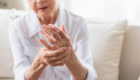 An elderly arthritis patient holding one hand with the other in a display of a flare-up