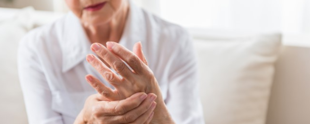 An elderly arthritis patient holding one hand with the other in a display of a flare-up