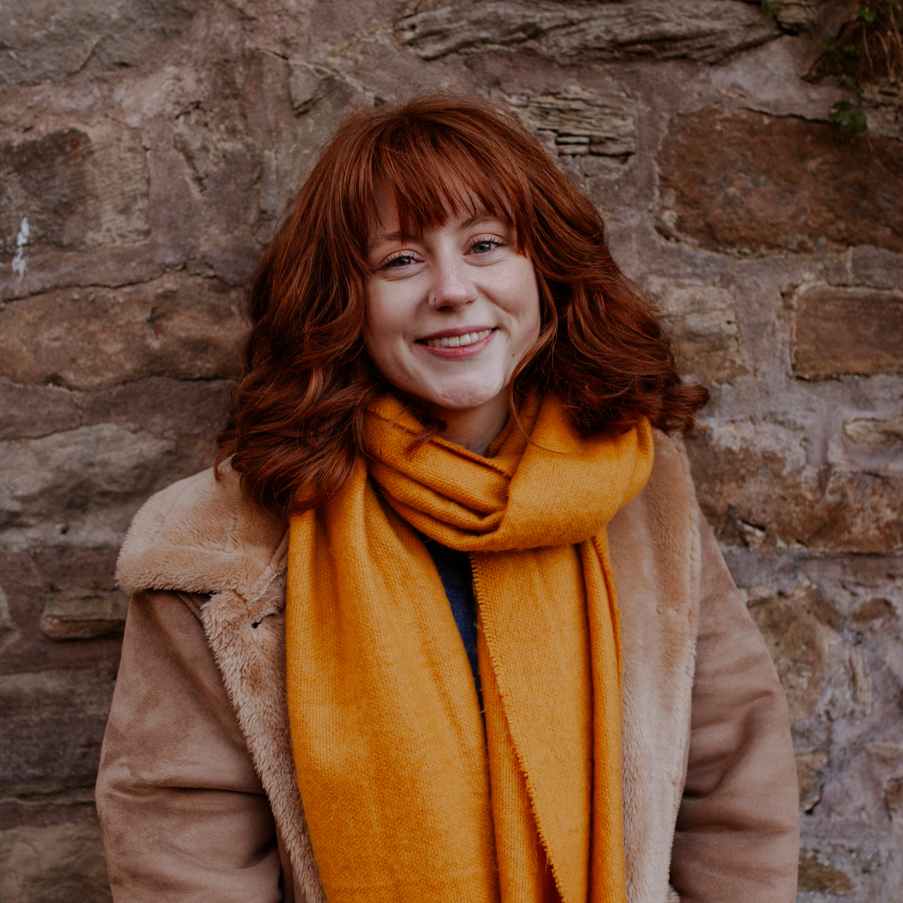 A woman in a yellow scarf standing in front of a wall