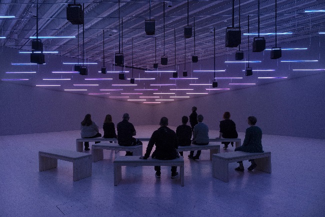 An image of people sitting in a light filled exhibition