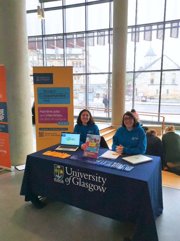 Two staff members sitting at the student opportunities hub stand.