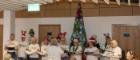 A choir sings in front of a knitted Christmas tree