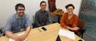 Three researchers sitting behind a table smiling to the camera.