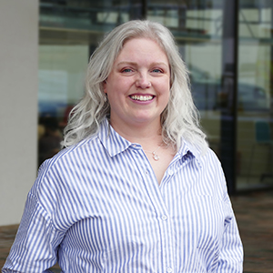 Profile photo of Lisa Chamberlain, standing outside the entrance of the Adam Smith Building, University of Glasgow