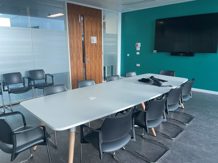 Flat floored teaching room with boardroom table and chairs, and video monitor.