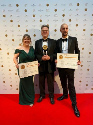 Three formally dressed individuals stand before a backdrop featuring