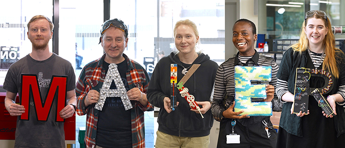 A group of give people holding up letters of the word MAKER