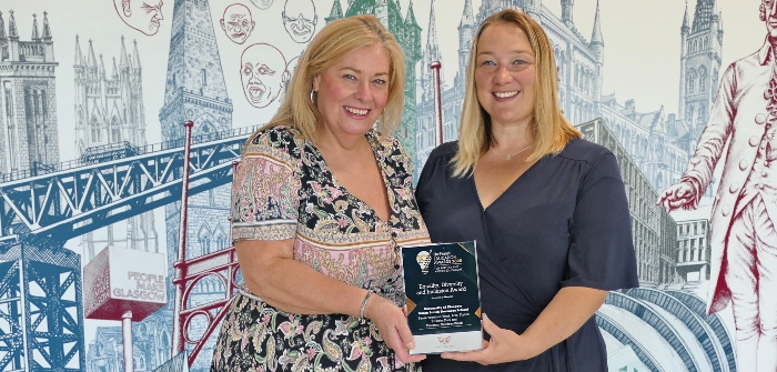 Professor Kathleen Riach and Kirsteen Daly standing in front of a wall mural in the Adam Smith Building, University of Glasgow, holding a Herald Education Awards 2025 award for winning Equality, diversity and inclusion award: Pause Together: Work, Live, Thrive
