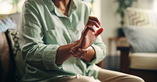 An image of a woman with arthritis holding one wrist with the other hand
