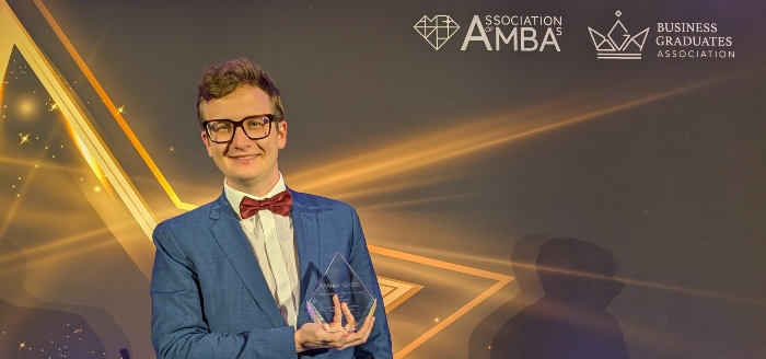 Jan Jasiński holding an award in front of a banner stand for AMBA and BGA Excellence Awards 2025