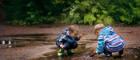 Two young boys are crouching down in a puddle of water playing