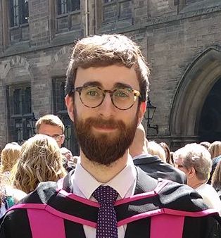 Portrait of a man with glasses in graduation robes.