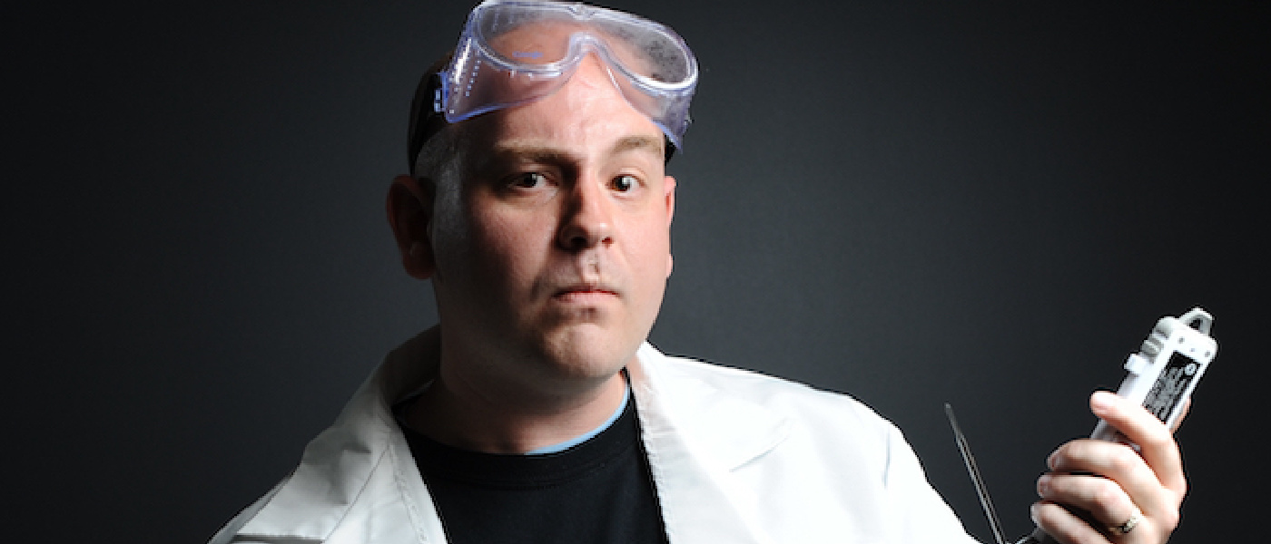Photo of Dr Jeff Dalton in a white lab coat posing with a piece of technological equipment