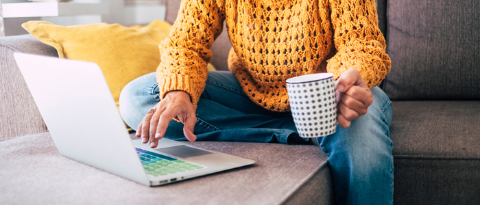 Photo of person in yellow jumper using laptop at home