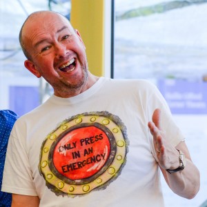 Photograph showing the author Alan Windram wearing a T Shirt that has an image of a button on it saying 'Only Press In An Emergency'.